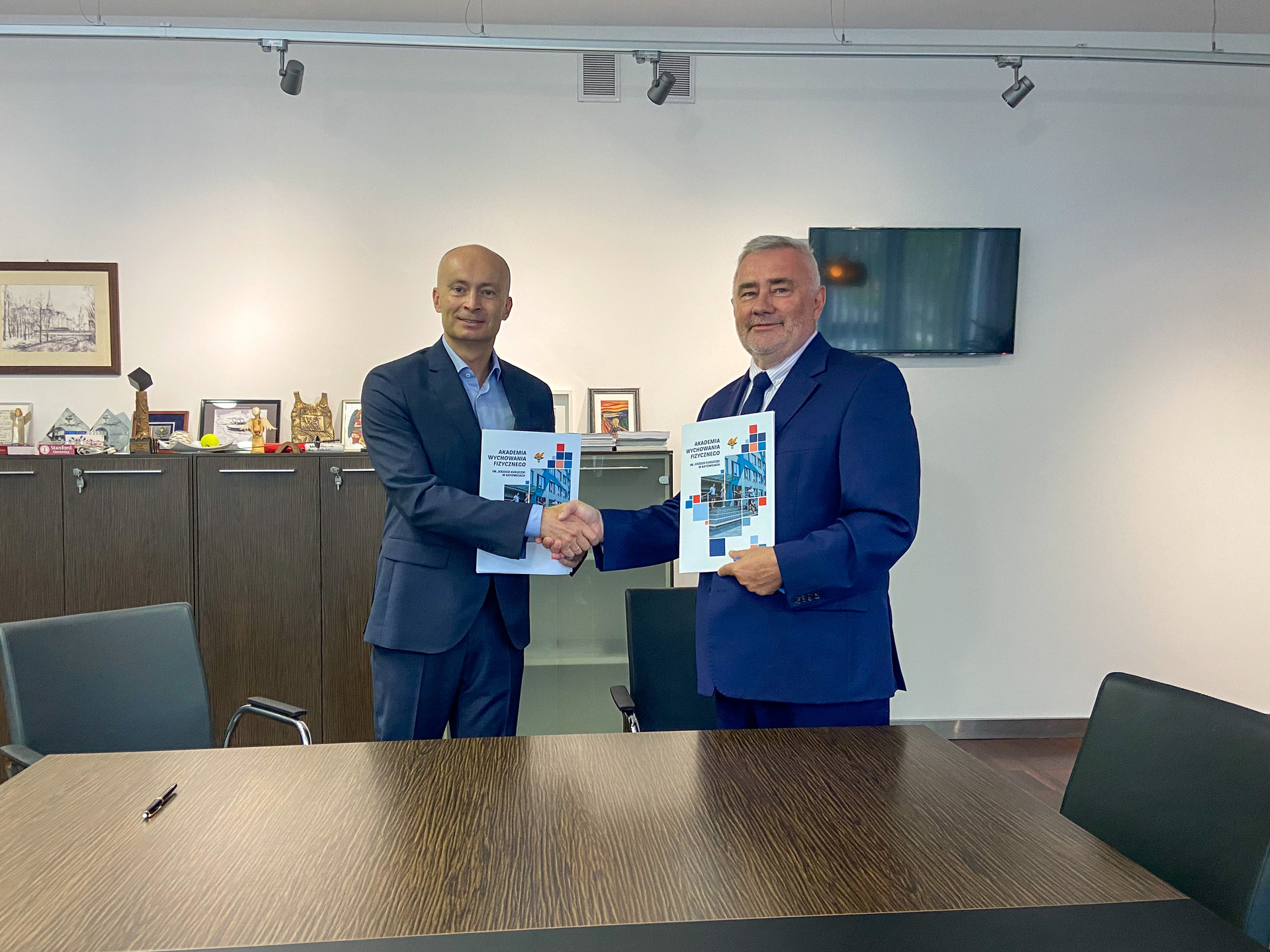 Zdjęcie przedstawia dwóch uśmiechniętych mężczyzn ściskających sobie ręce