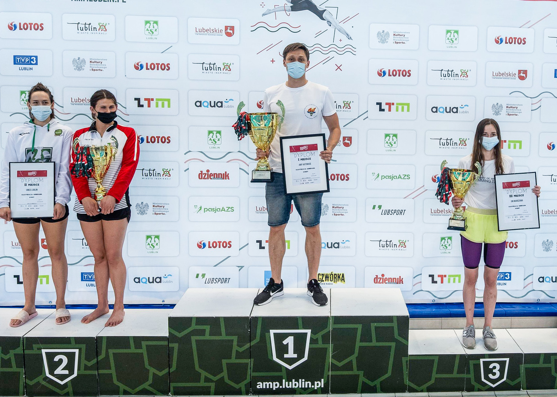 Zdjęcie przedstawia ludzi stojących na podium z nagordami