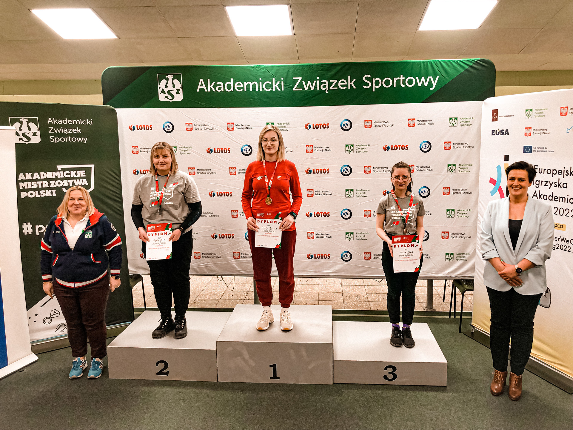 Zdjęcie przedstawia grupę osób stojących na podium z nagrodami