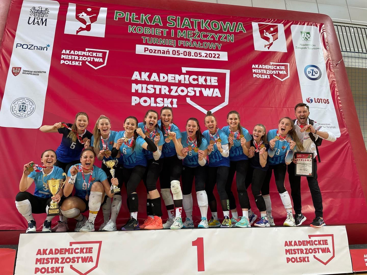 Zdjęcie przedstawia grupę ludzi uśmiechających się stojących na podium 1. miejsca